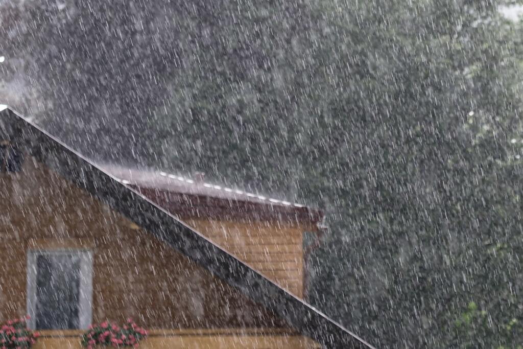 Heavy rain falling on house roof with gutters during intense storm weather
