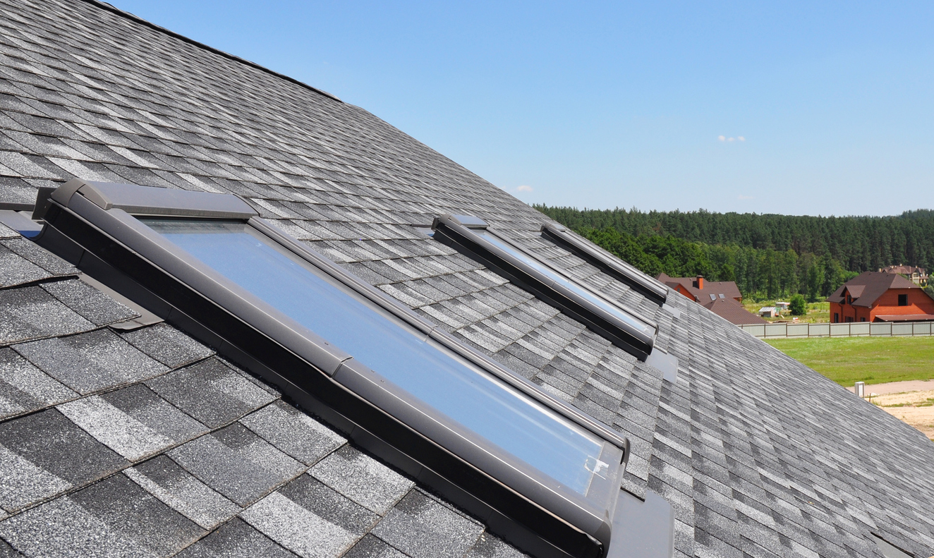 Modern roof skylights installed on gray shingle roof with residential homes visible
