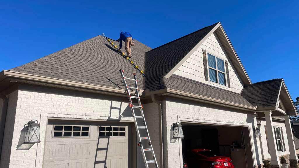 Professional roofer working on residential home roof repair with ladder and tools