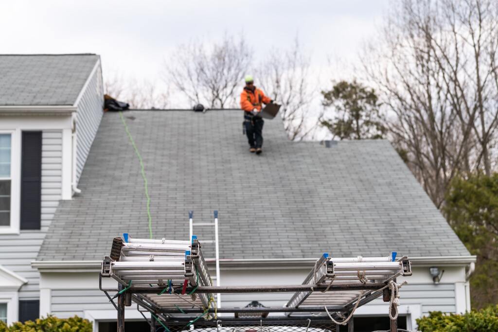 Construction worker in orange safety vest working on gray shingle roof repair