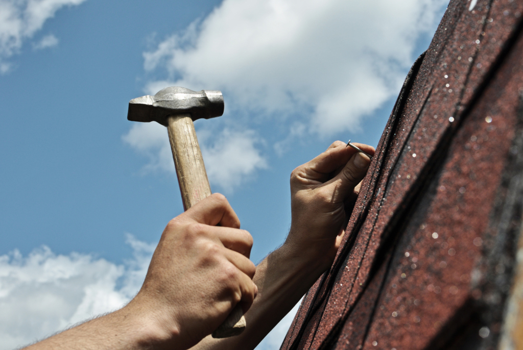 Person's hands holding hammer for roof repair work against blue sky with clouds