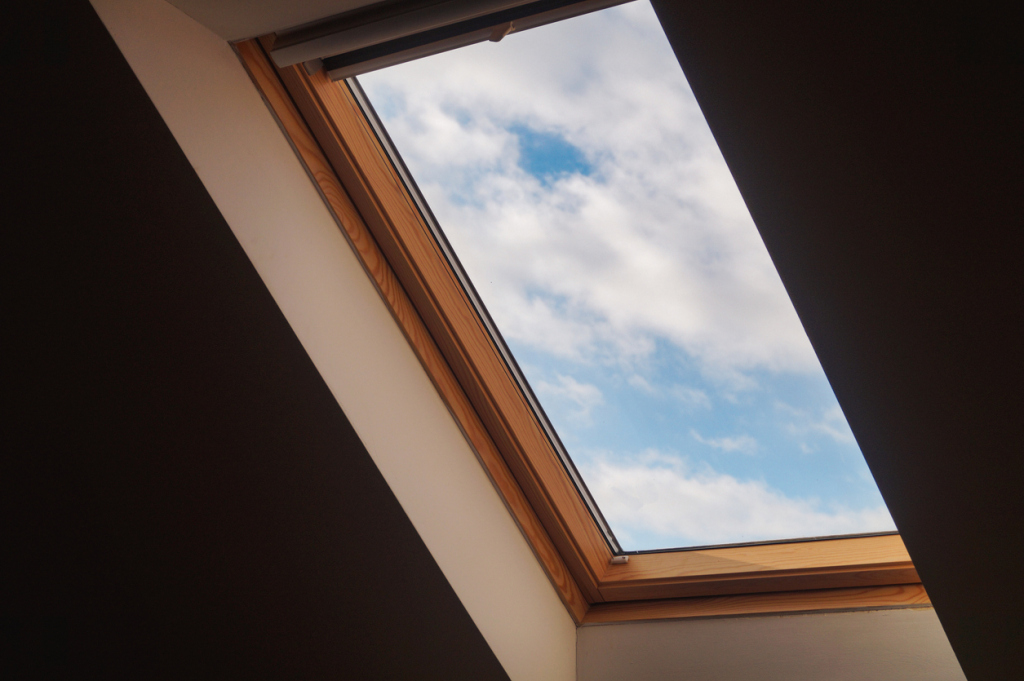 Wooden frame skylight window showing blue sky with white clouds from interior view