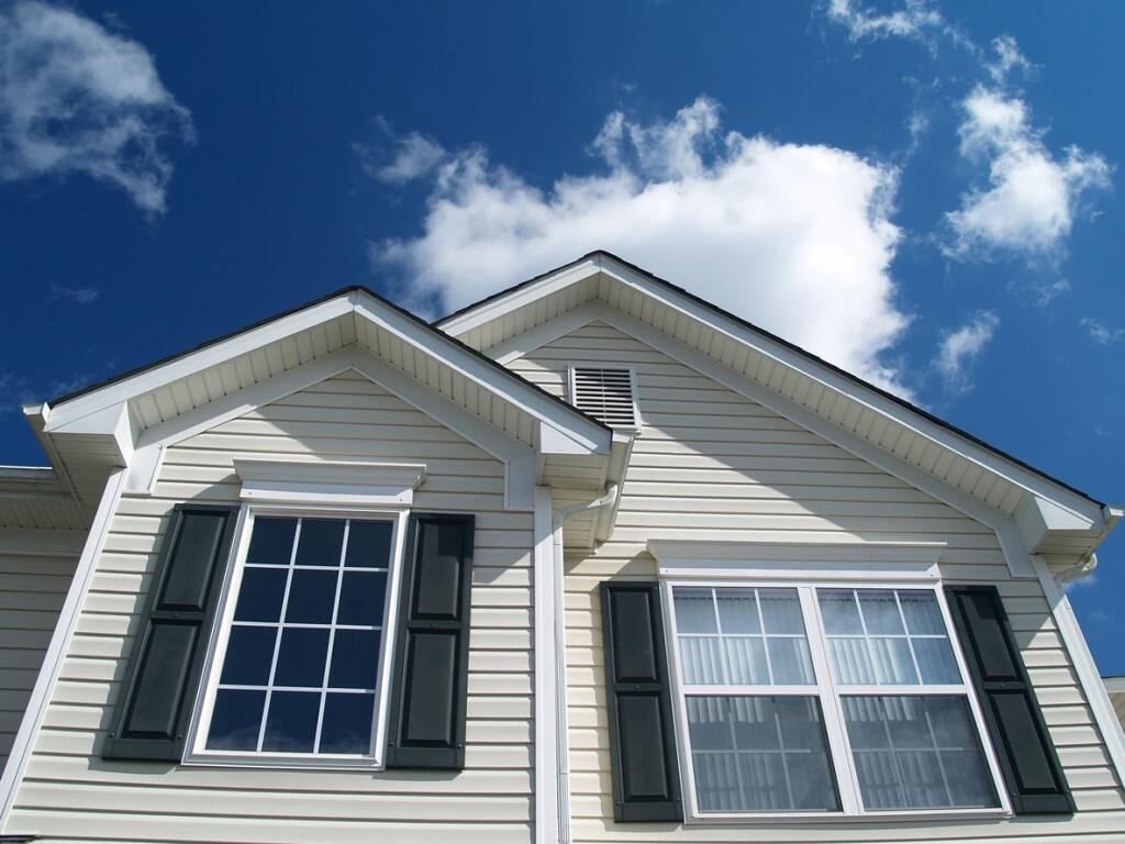 Modern beige vinyl siding house exterior with dark green shutters against blue sky